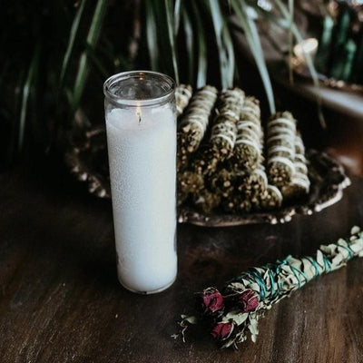 white seven day candle next to herb bundle
